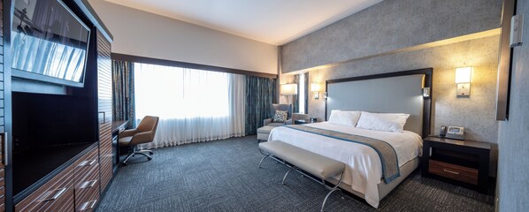 A hotel room with a large bed, a desk, a chair, and a TV.