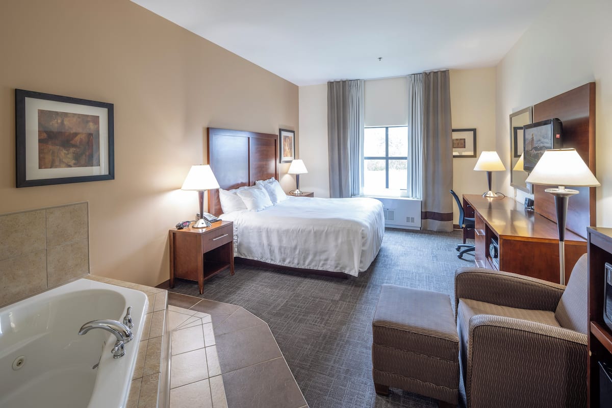A hotel room with a large bed, two bedside tables with lamps, a desk with a chair, a television, and a bathroom with a bathtub and shower.