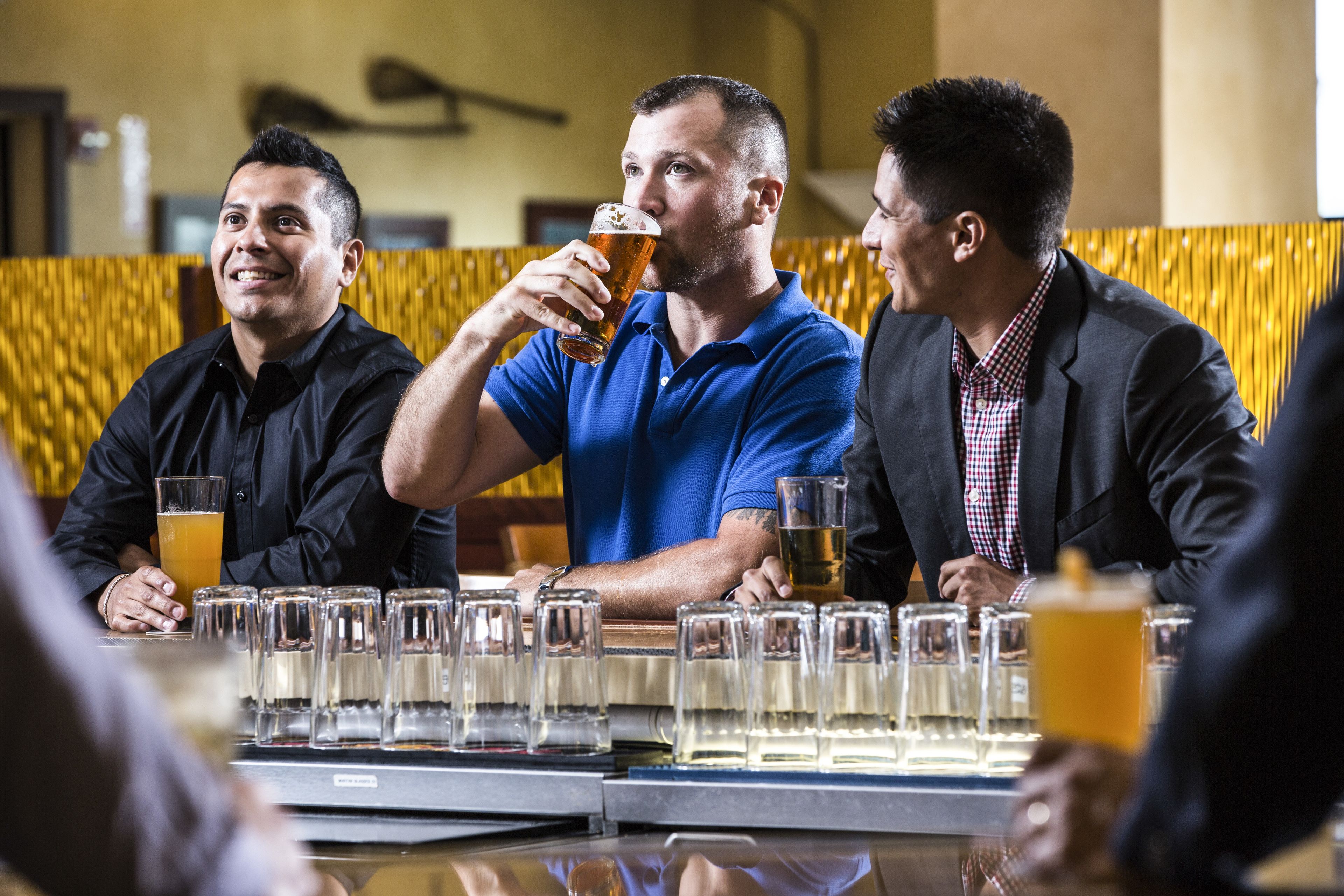 A bar setting with multiple glasses of beer and a person drinking from a glass.