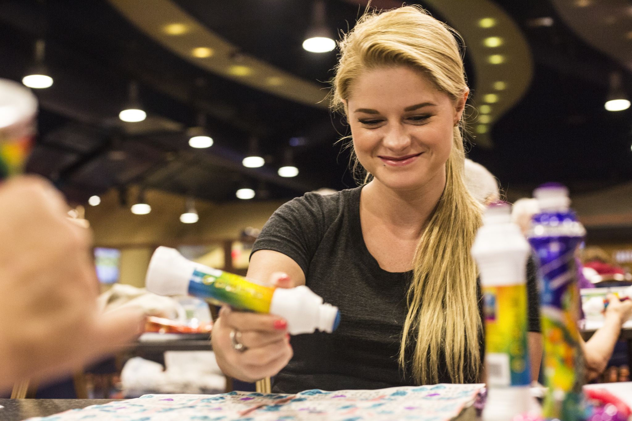 A person holding a bottle of glue at a table with a colorful tablecloth.