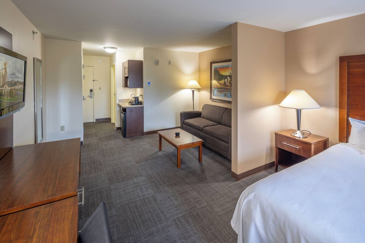 A hotel room with a bed, a sofa, a desk, a lamp, and a painting on the wall.