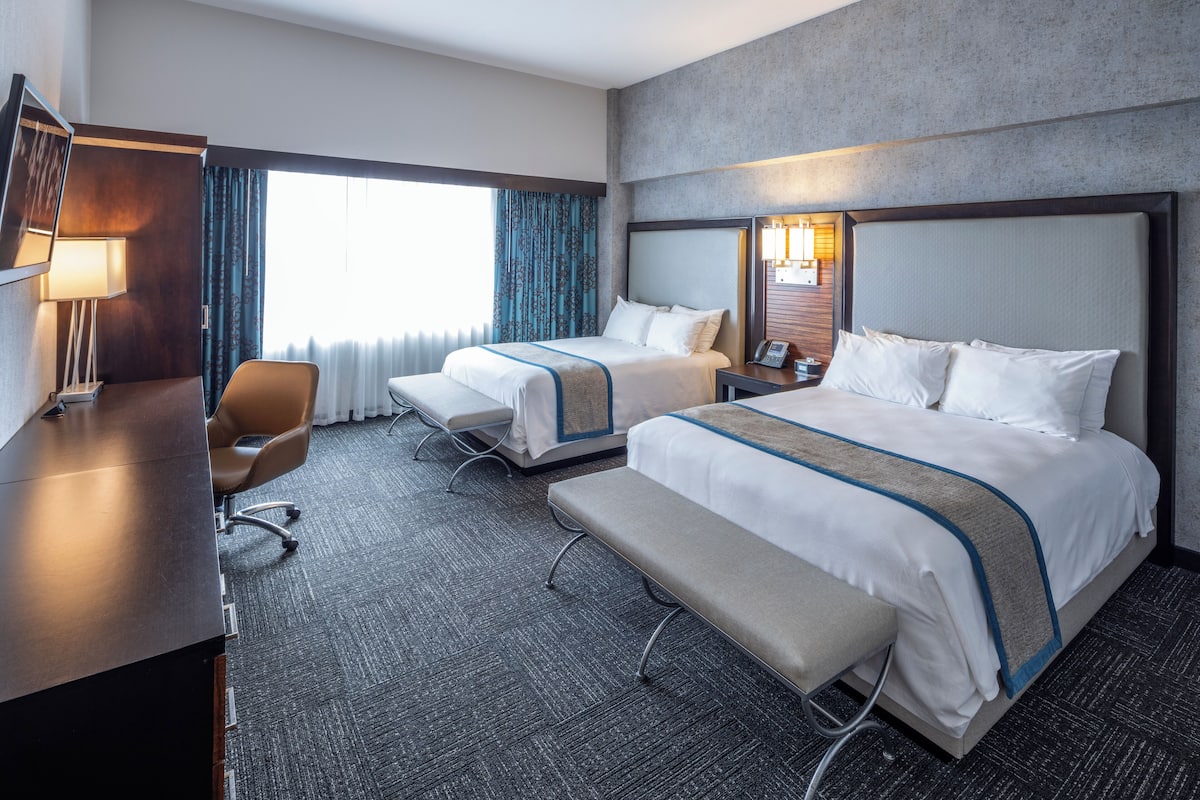 A hotel room with two beds, a desk, a chair, and a bench.