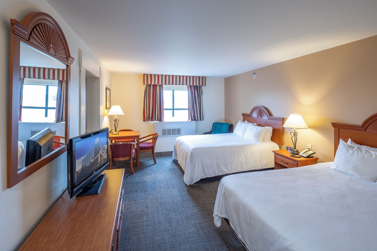 A hotel room with two beds, a desk with a TV, a chair, and a window with curtains.