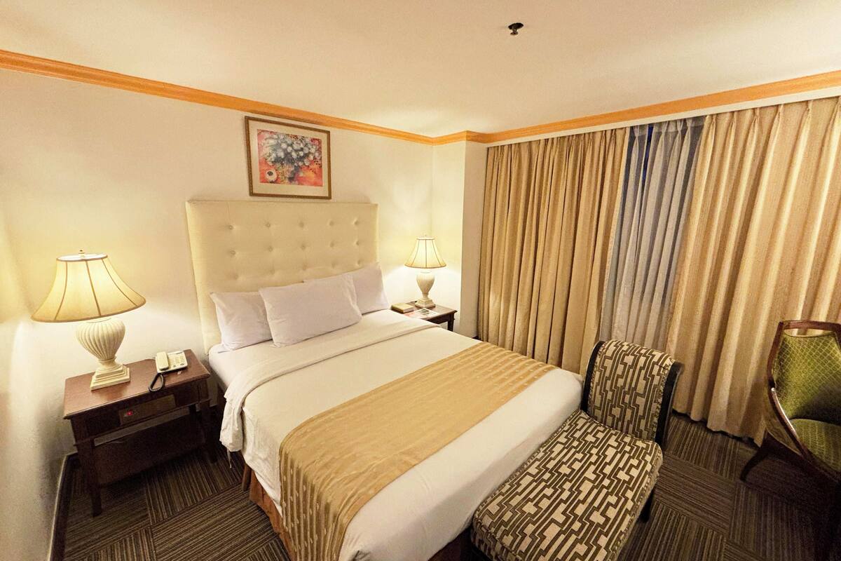 Habitación de hotel con una cama grande, dos lámparas de noche, una silla y una ventana con cortinas.