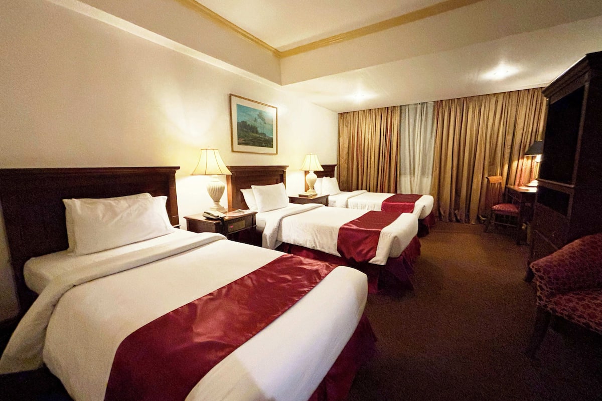 Habitación de hotel con tres camas, un televisor y un cuadro en la pared.