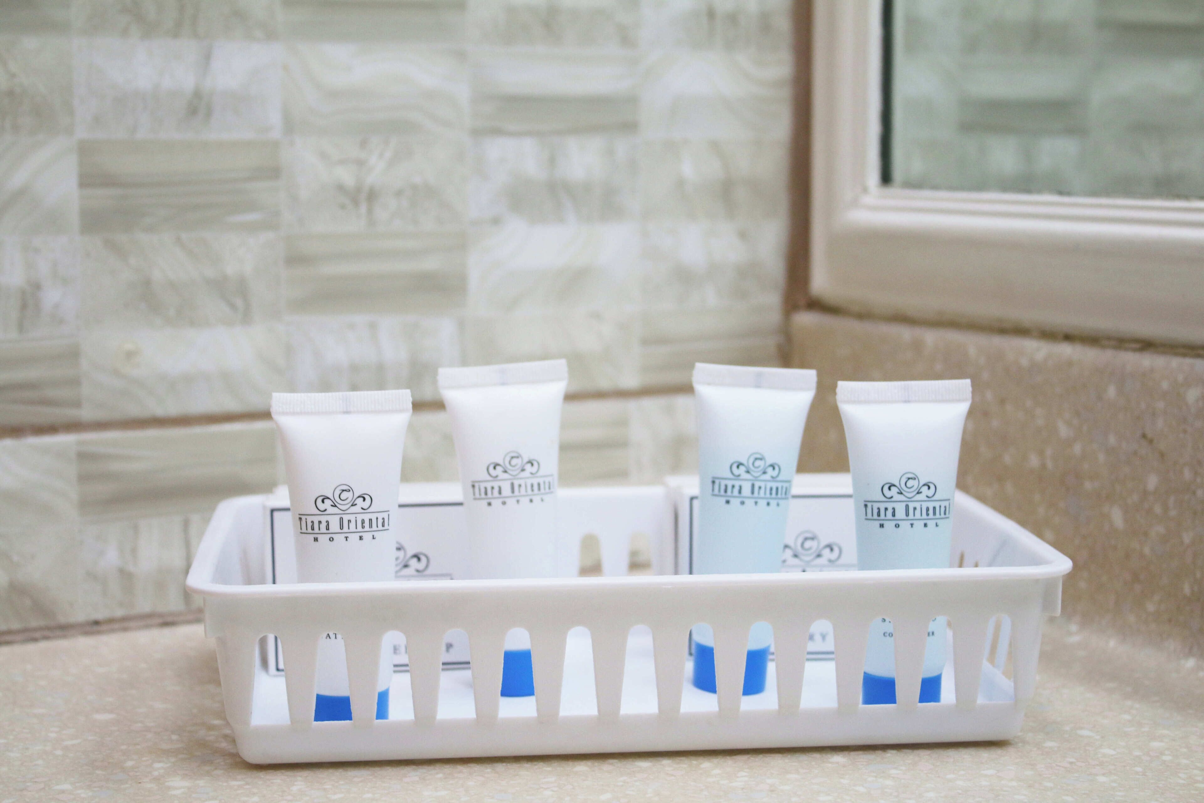 A white plastic basket containing four white tubes with blue caps, labeled "Tiara Oriental Hotel."