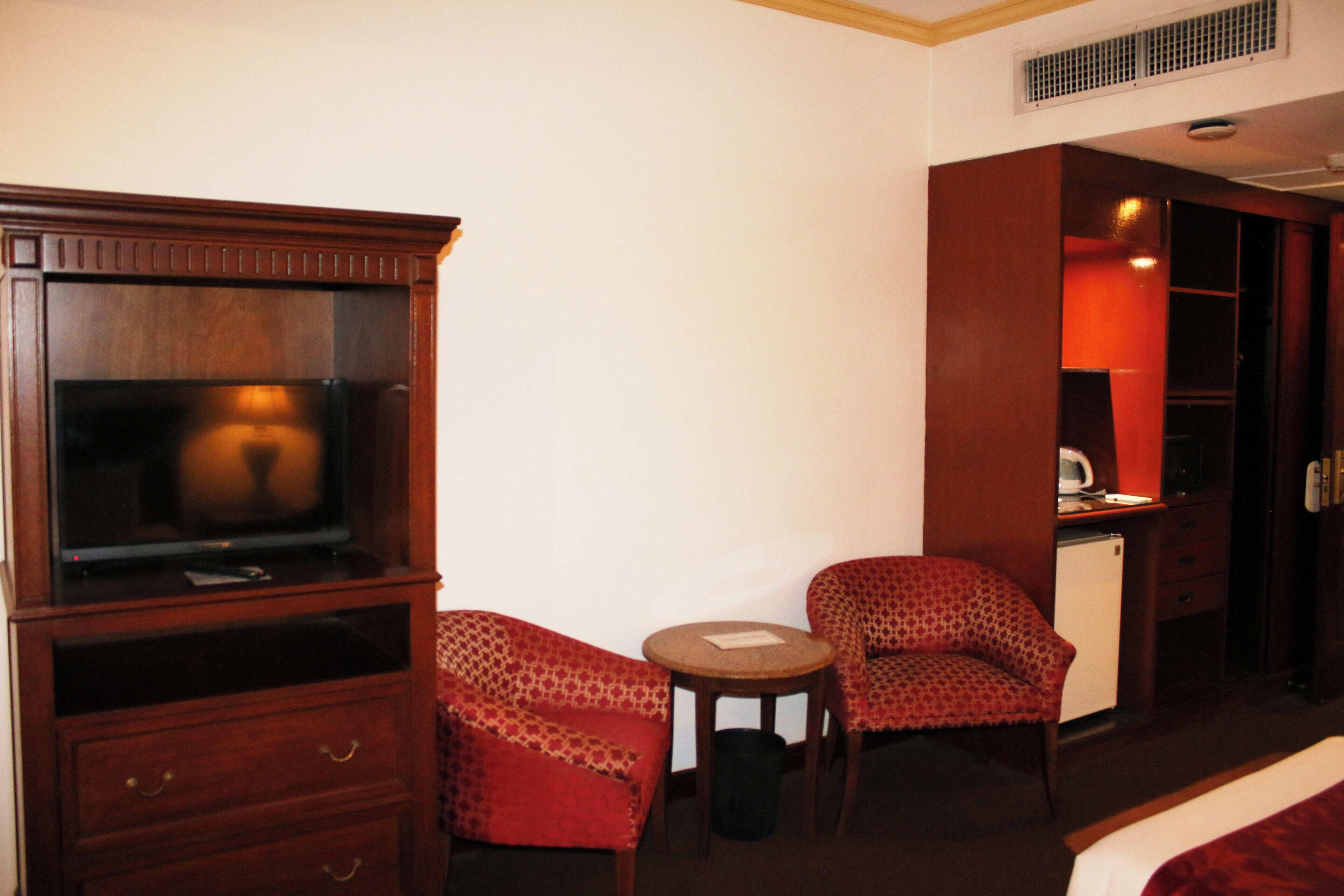 A hotel room with a television, two patterned chairs, a small table, a desk, and a bed.