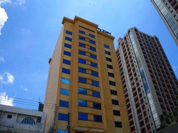 Un edificio alto amarillo con múltiples ventanas y balcones, junto a un edificio rojo más alto.
