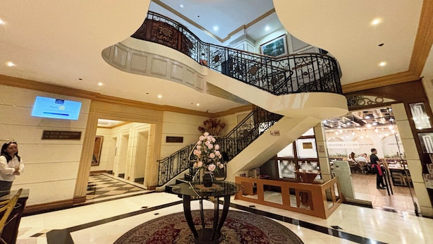 A grand lobby with a central staircase, a reception desk, and a dining area visible in the background. - Tiara Oriental Hotel Makati powered by Cocotel (Makati)