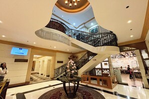 Un amplio vestíbulo con una escalera central, un mostrador de recepción y un comedor visible al fondo.