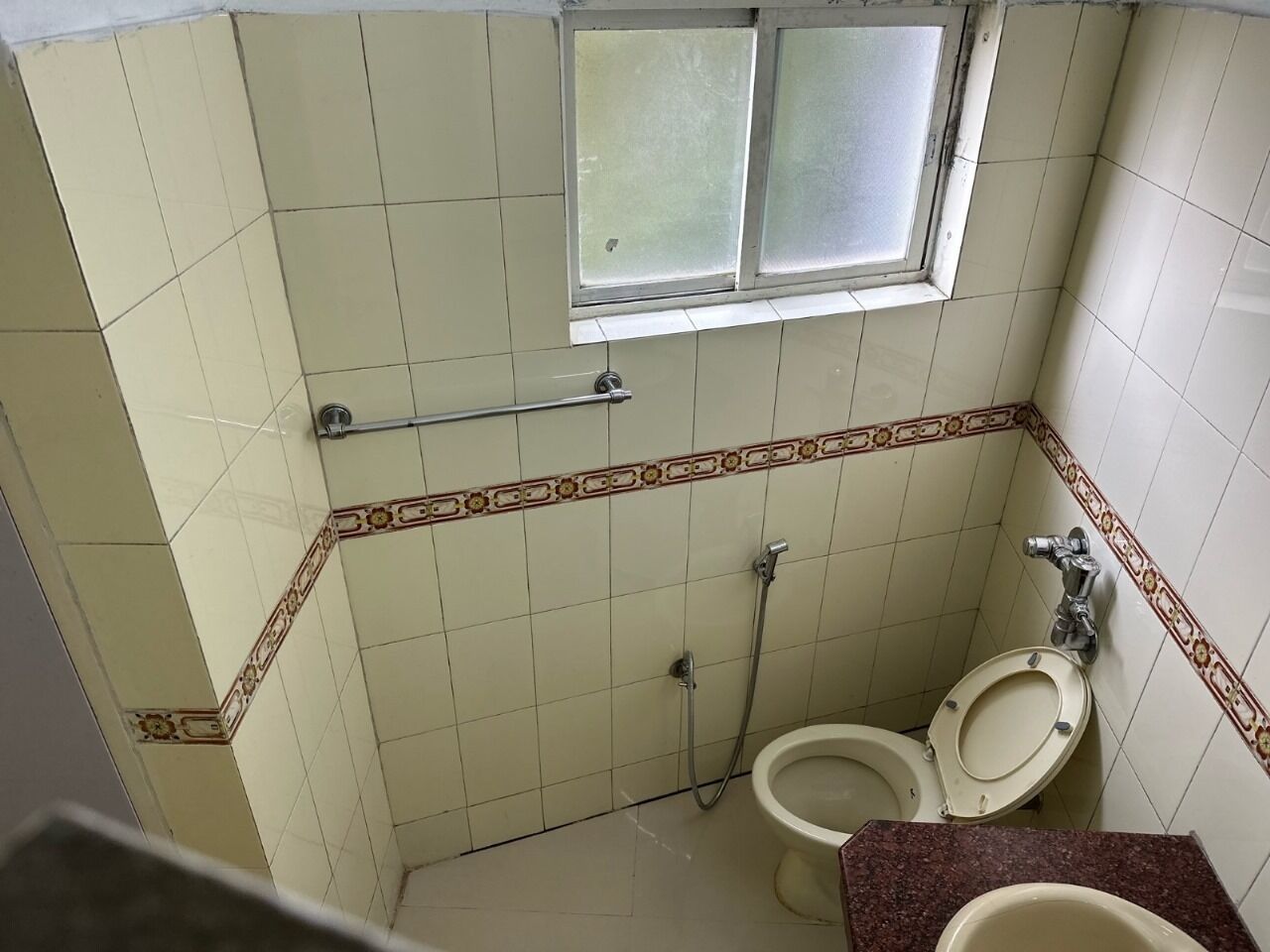 Een kleine badkamer met twee toiletten, een douche en een raam.