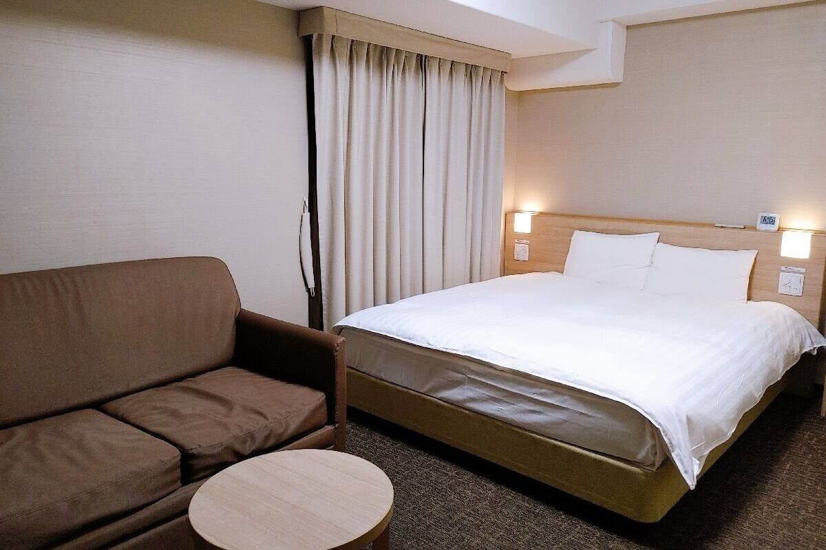 A hotel room with a bed, a brown sofa, and a small round table.
