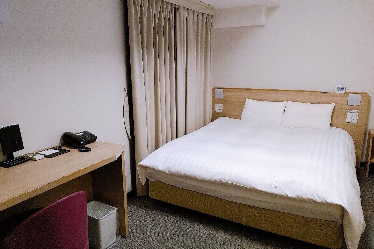A hotel room with a single bed, a desk with a telephone, and a chair.