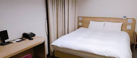 A hotel room with a single bed, a desk with a telephone, and a chair.