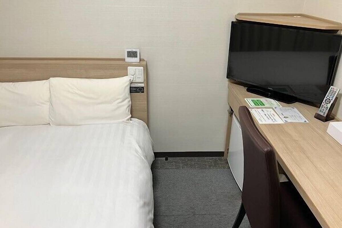 A hotel room with a bed, a desk with a television, and a small refrigerator.