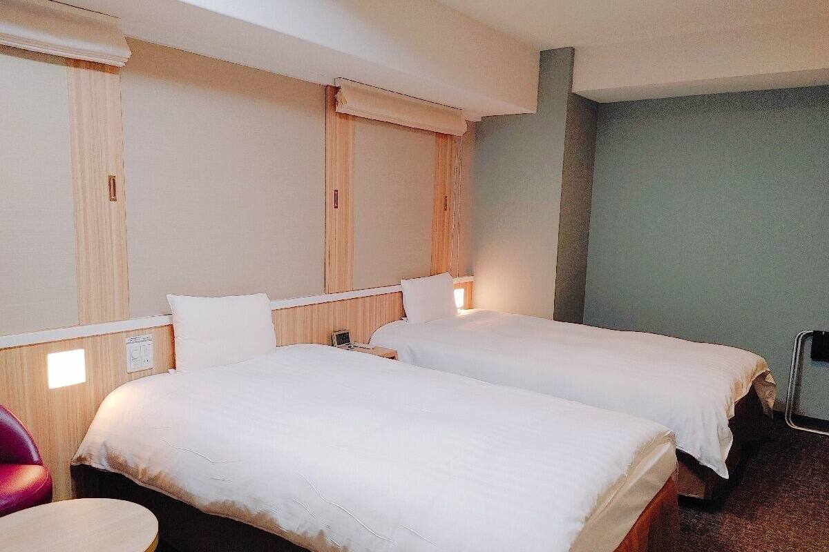 A hotel room with two beds, a small round table, and a chair.