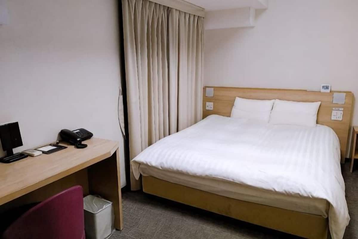 A hotel room with a bed, a desk with a chair, a telephone, and a trash bin.