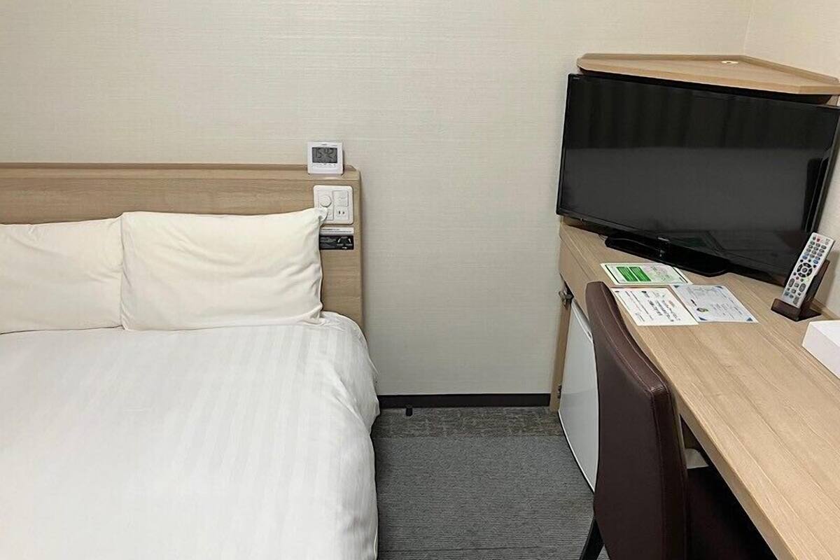 A hotel room with a bed, a desk with a television, and a small refrigerator.