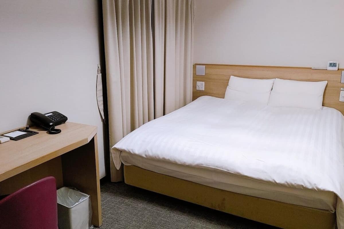 Une chambre d’hôtel comprenant un lit, un bureau avec un téléphone, une chaise et une poubelle.