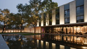Un edificio moderno con piscina reflectante, grandes ventanales y mobiliario exterior.