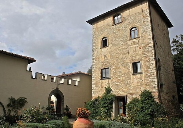 A stone building with a tower, an arched entrance, and surrounding greenery.