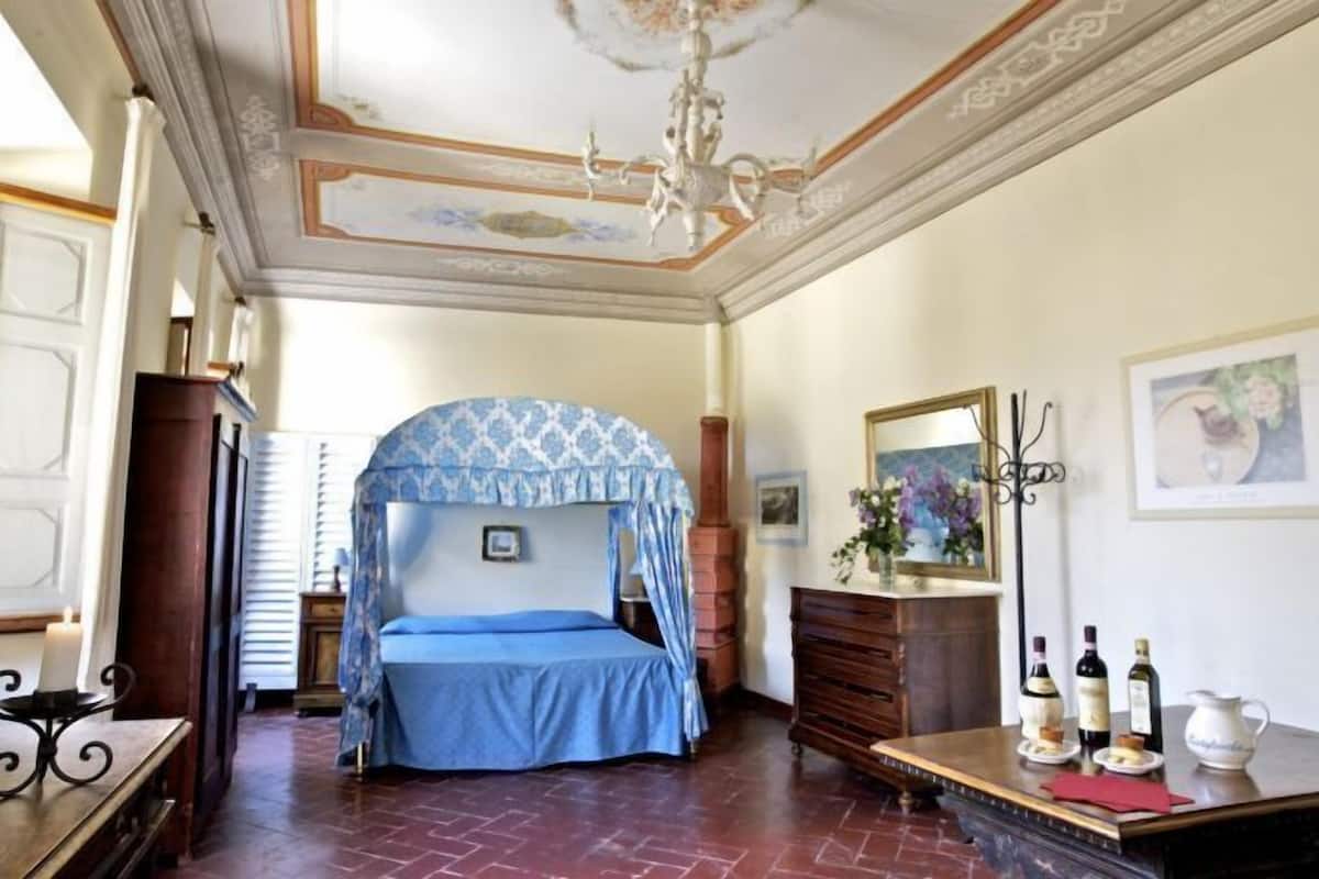 Un dormitorio con cama a dosel, muebles de madera, un candelabro y obras de arte en las paredes.