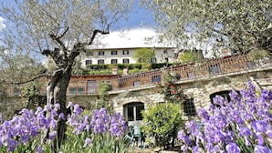 Un edificio de piedra con balcón que da a un jardín con flores moradas.