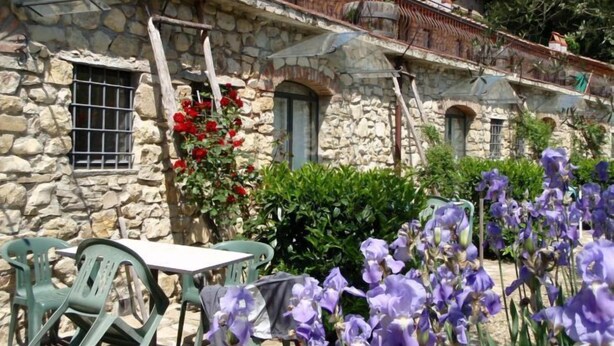 Un edificio de piedra con un balcón, una ventana con rejas y una mesa con sillas afuera.