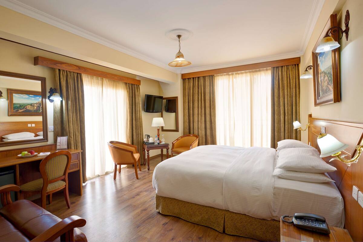 Une chambre d’hôtel avec un grand lit, un bureau avec une chaise, une télévision et une lampe de bureau.
