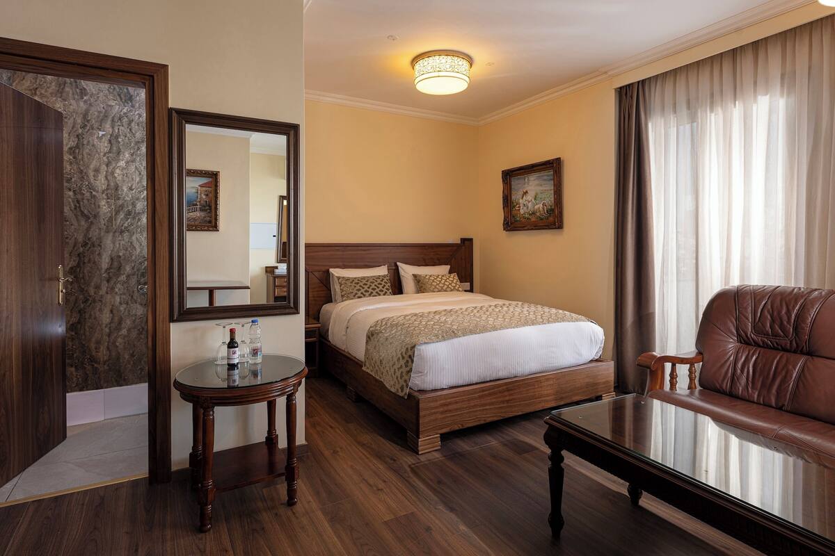 Une chambre d’hôtel avec un lit en bois, une table ronde, un canapé en cuir et un grand miroir.