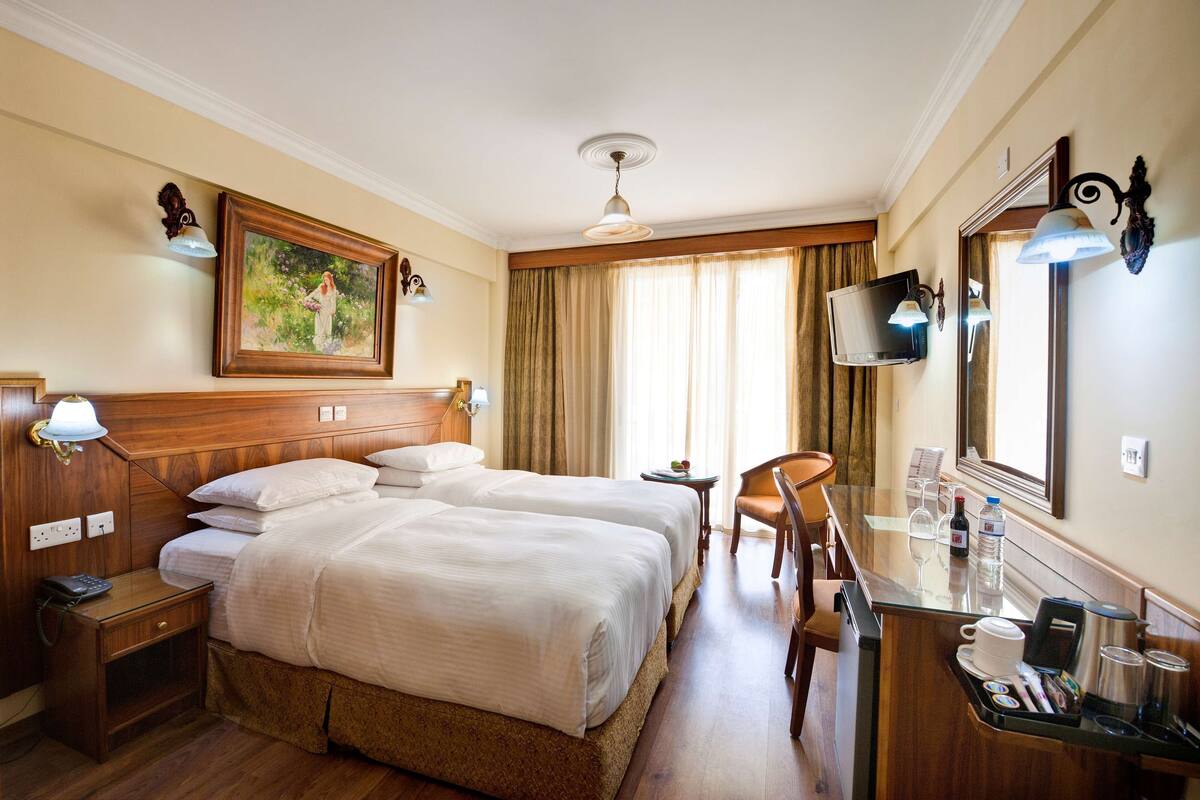 Une chambre d’hôtel avec deux lits, un bureau avec une chaise, une télévision et un tableau au mur.