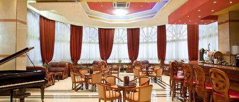 A spacious lobby with a grand piano, comfortable seating, and a bar area.