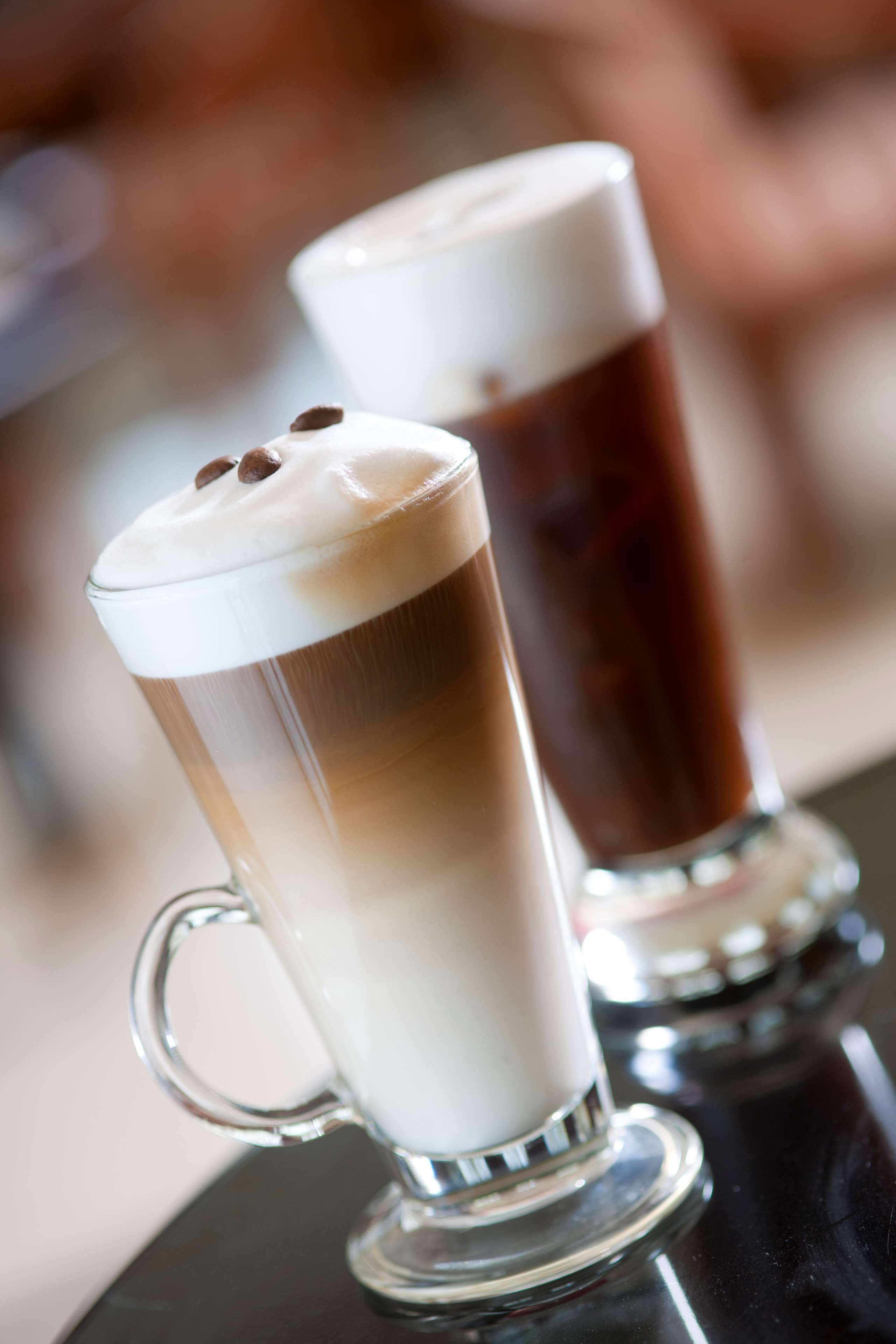 Zwei hohe Gläser Eiskaffee mit Schlagsahne und Schokoladenstückchen auf einer spiegelnden Oberfläche.