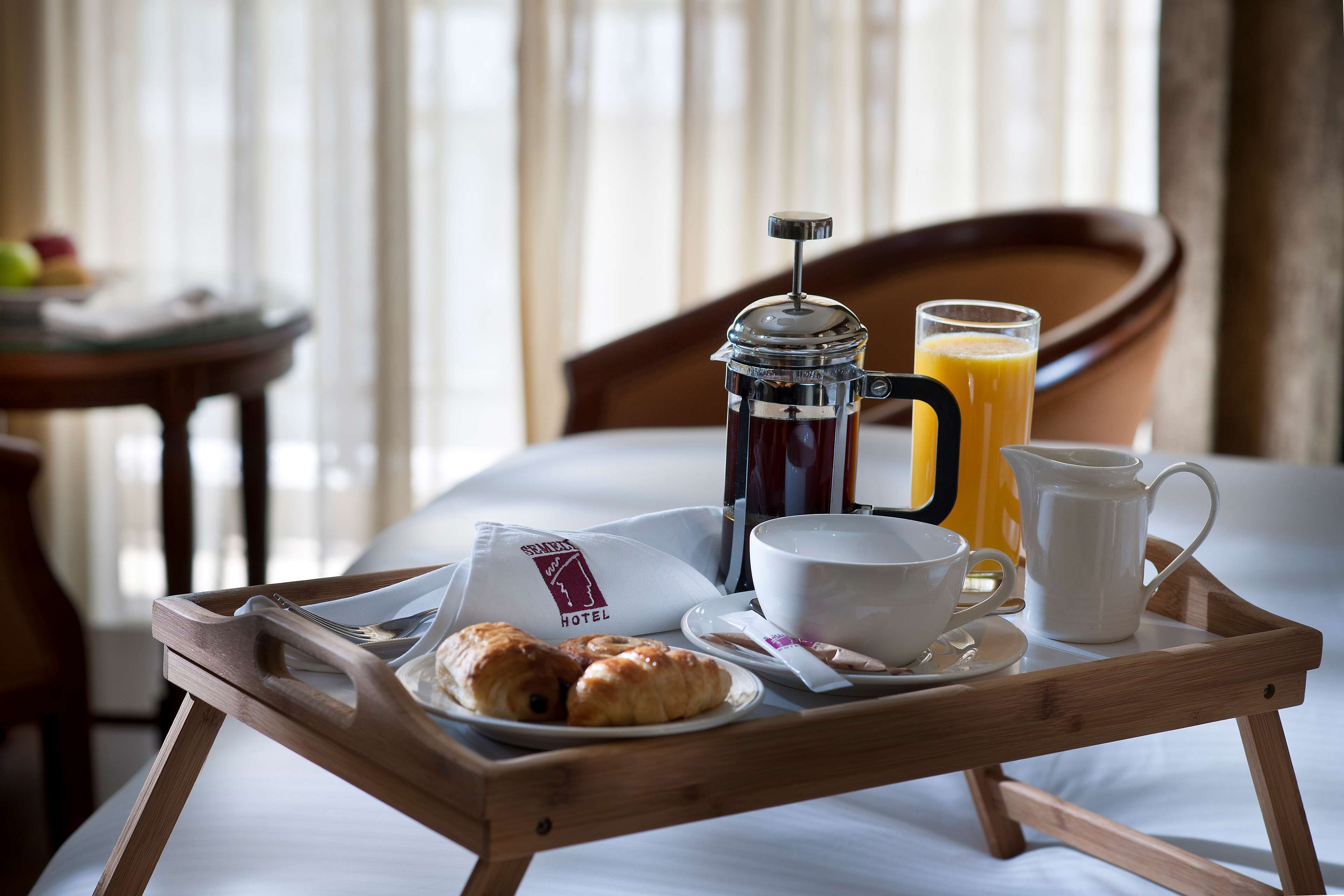 Bandeja de desayuno con cruasanes, café, zumo de naranja y una almohada de hotel sobre una cama.