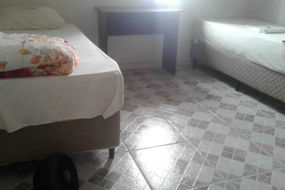 A small, clean room with two beds, a nightstand, and tiled flooring.