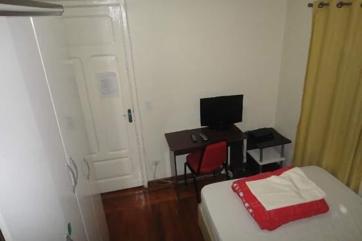 A small, simple room with a bed, a desk with a computer, and a door.