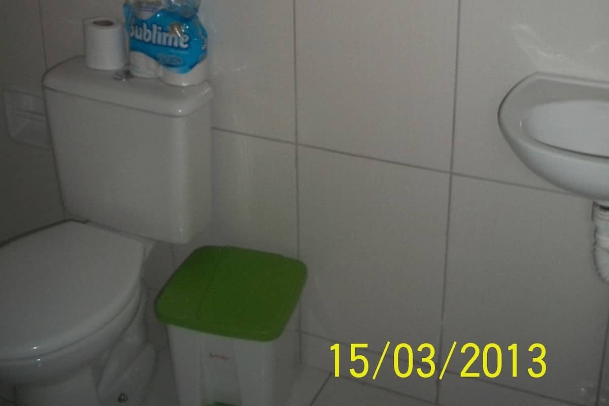 A bathroom with a toilet, a green trash bin, and a sink.