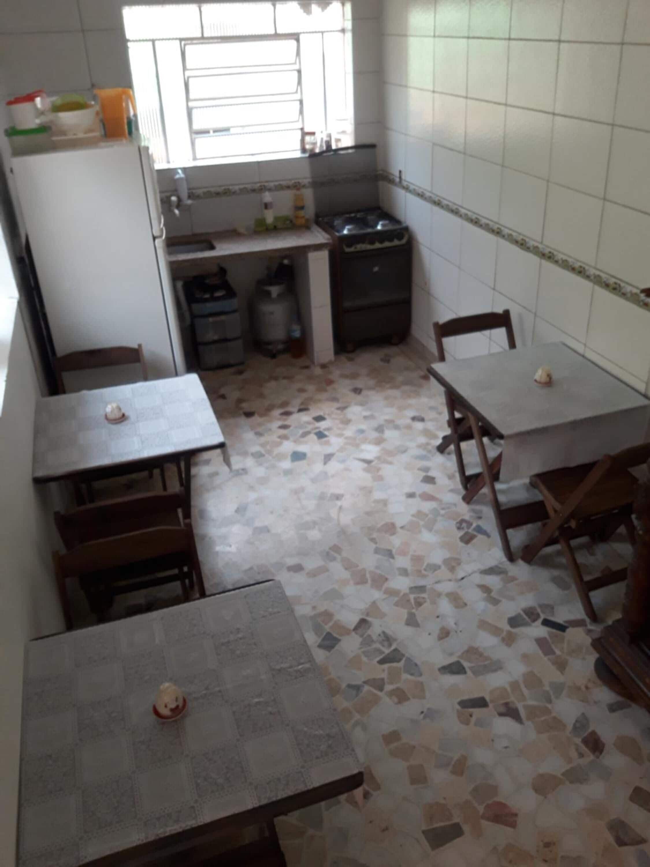 A small kitchen with a tiled backsplash, a gas stove, a sink, and a window. There are two wooden tables with chairs.