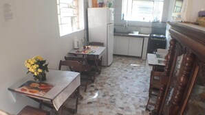 Eine Küche mit Fliesenboden, einem Esstisch mit Stühlen, einem Kühlschrank und einer Mikrowelle.