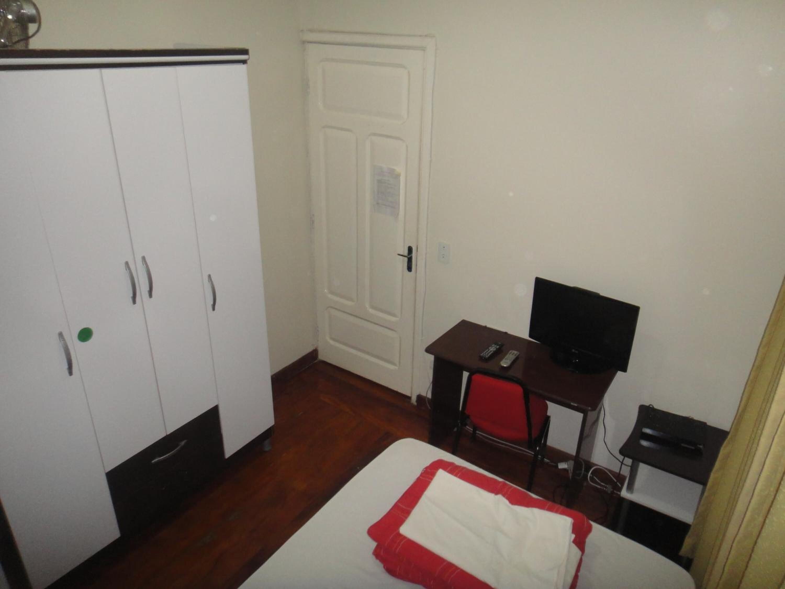 Une pièce comprenant un lit, un bureau avec un ordinateur, une chaise, une armoire et une porte.