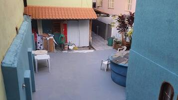Um pátio com um pequeno edifício, mobiliário externo e uma parede azul.