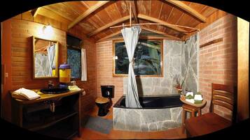 A rustic bathroom with a wooden vanity, a black bathtub, and a stone shower enclosure.