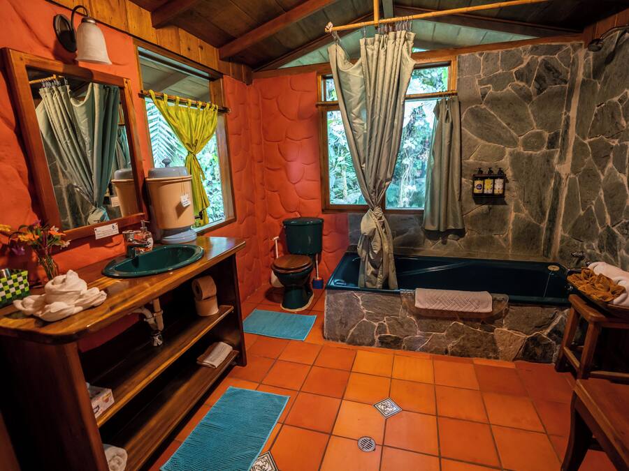 Une salle de bain avec un mur en pierre, une baignoire, des toilettes, un lavabo et un miroir.