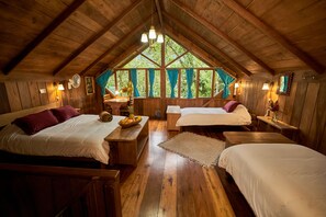 A cozy cabin with wooden walls and a sloped ceiling, featuring two beds, a dining table, and a large window with curtains. - Casa Divina Eco Lodge (Mindo)