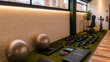 Een sportschool met trainingsapparatuur, een groene fitnessmat en uitzicht op gebouwen door grote ramen.
