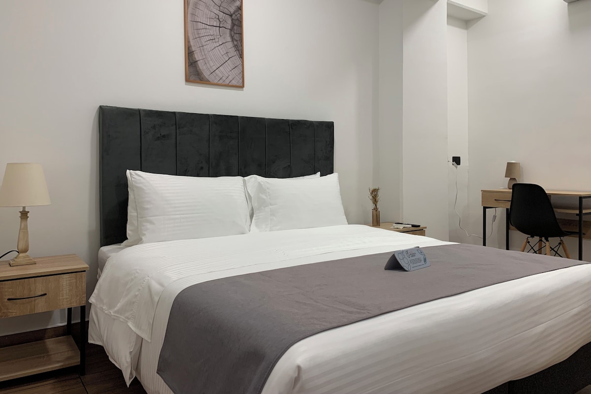 Una habitación de hotel con cama, escritorio, silla, lámpara y un cuadro en la pared.