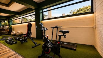 Un gimnasio con equipo de ejercicio, cinta de correr y vistas a edificios a través de amplios ventanales.