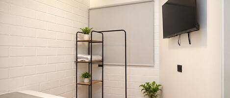 Un dormitorio con una cama, un televisor de pared, una estantería con plantas y una ventana con persiana.