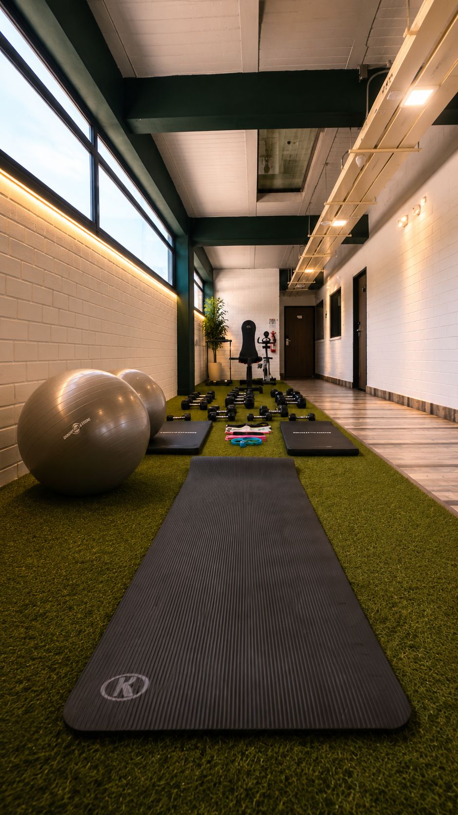 Academia com equipamentos de ginástica, tapete de yoga e bicicleta ergométrica na parede.