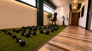 Un gimnasio con equipo de ejercicio, un soporte de mancuernas en la pared y piso de madera.